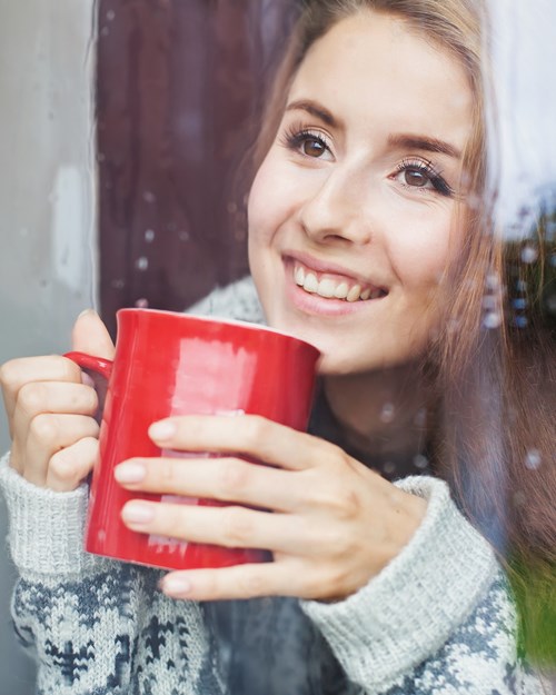 Woman looking out the window with a hot drink