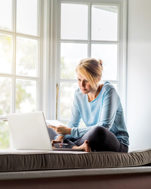 Young woman using laptop on window sill