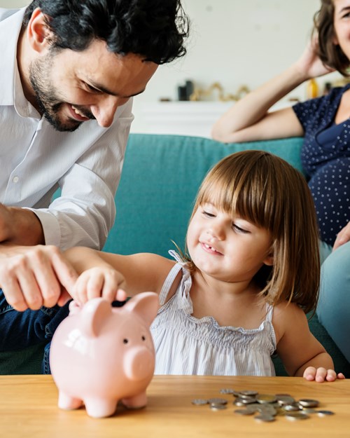 young girl putting coins into a piggy bank with parents